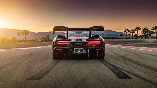 A McLaren Senna is parked on a track with palm trees and mountains in the background during sunset, 4K Desktop Wallpaper
