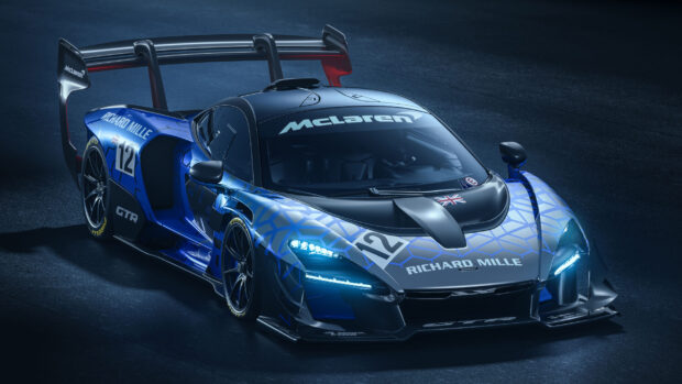 A blue McLaren Senna with detailed decals and illuminated headlights on a dark track, 2K Desktop Wallpaper