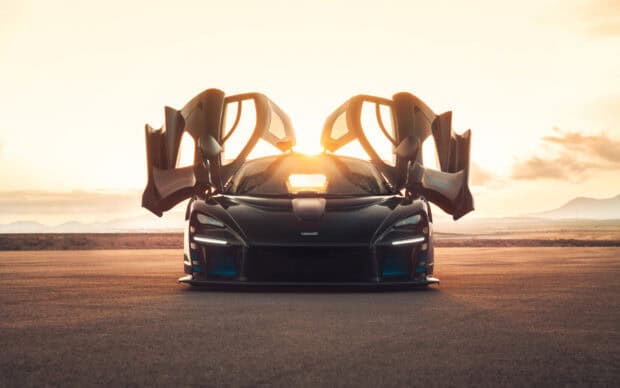 A black McLaren Senna is parked on a road with its gullwing doors open at sunset, HD Desktop Wallpaper