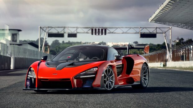 A red Mclaren Senna racing car is parked on a professional race track under a cloudy sky, 4K Desktop Wallpaper