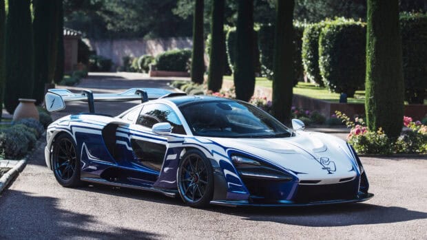 A McLaren Senna is parked on a driveway surrounded by tall trees and shrubs, 4K Desktop Wallpaper