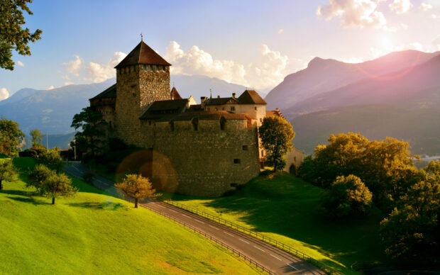 A medieval stone castle stands surrounded by green fields and mountains in Liechtenstein, 2K Desktop Wallpaper