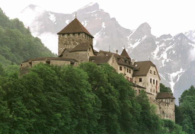A medieval castle is surrounded by dense green forest with snowy mountains in the background in the Liechtenstein Wallpapers, HD Desktop Wallpaper