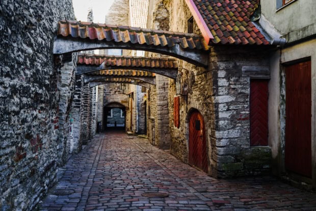 A cobblestone medieval street with stone walls and red wooden doors in Estonia featuring Estonia wallpapers, 2K Desktop Wallpaper