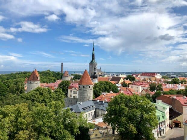 A panoramic view of Estonia with medieval towers and lush greenery under a partly cloudy sky, HD Desktop Wallpaper