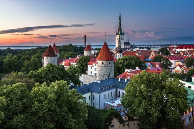 A beautiful Estonia cityscape with medieval towers and lush greenery under a colorful sunset sky, HD Desktop Wallpaper