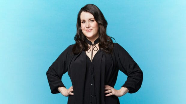 Melanie Lynskey stands confidently against a blue background wearing a black outfit, HD Desktop Wallpaper