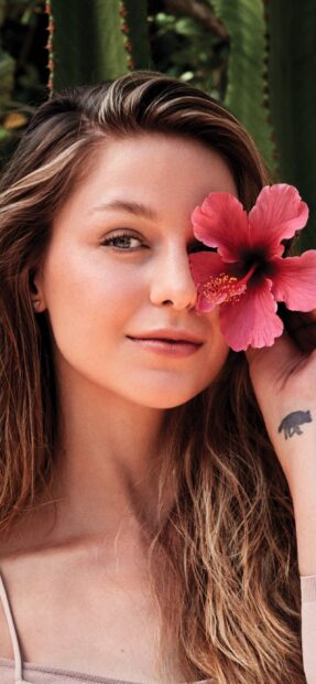 A close up of Melissa Benoist holding a pink flower near her face in a natural setting, 2K Mobile Wallpaper
