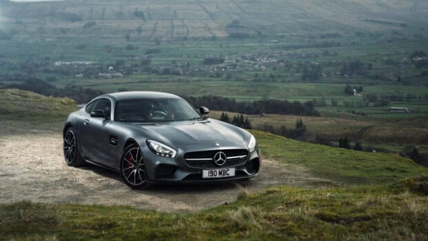 A Mercedes Benz AMG GT is parked on a hill overlooking a green valley under a cloudy sky, 4K Desktop Wallpaper