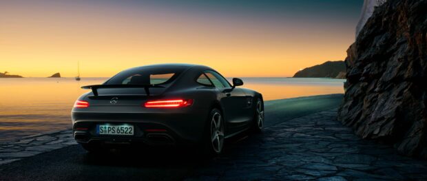 A Mercedes Benz Amg Gt is parked near a rocky coastline during a vivid sunset, 2K Desktop Wallpaper