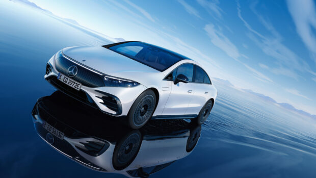A silver Mercedes Benz Eqs is reflected on a calm water surface under a blue sky, 2K Desktop Wallpaper
