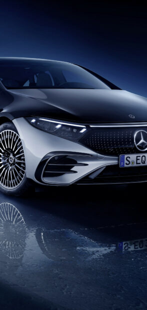 A Mercedes Benz EQS with illuminated headlight and detailed front grille is parked reflecting on wet ground, HD Mobile Wallpaper