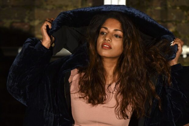 A confident Mia rapper adjusts her dark jacket while looking away thoughtfully, HD Desktop Wallpaper