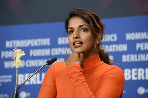 Mia rapper in a bright orange top speaking at a press event, 2K Desktop Wallpaper