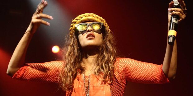 Mia rapper wears sunglasses and an orange outfit while holding a microphone, 2K Desktop Wallpaper