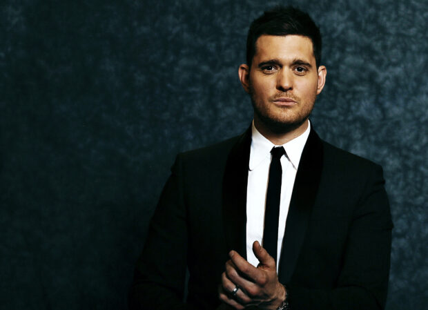 Michael Buble stands confidently in a dark suit against a blue textured background, HD Desktop Wallpaper