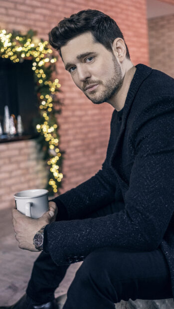 Michael Buble is sitting indoors holding a cup near Christmas lights, 2K Phone Wallpaper