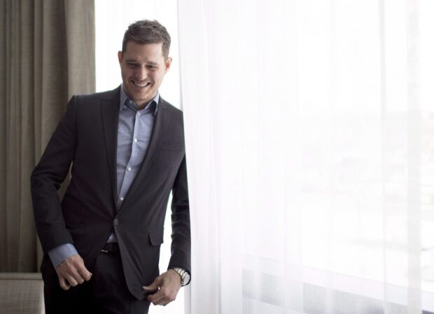 Michael Buble is smiling while adjusting his suit near a window with light curtains, HD Desktop Wallpaper