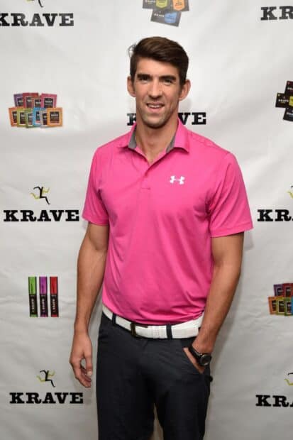 Michael Phelps stands smiling in a casual pink shirt and black pants at the Krave event, HD Mobile Wallpaper