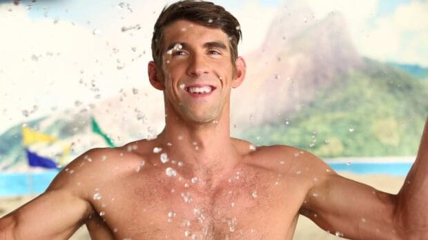 Michael Phelps is smiling joyfully with water splashing around him on a beach, HD Desktop Wallpaper