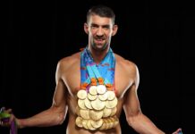Michael Phelps is shown smiling wearing many Olympic gold medals around his neck against a black background, HD Desktop Wallpaper