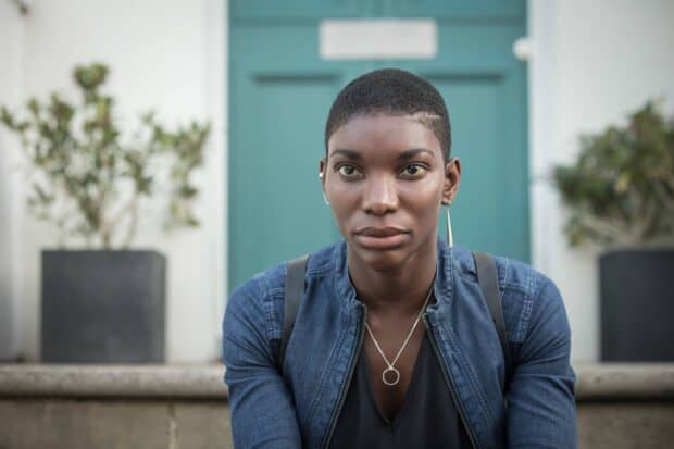 A close up portrait of Michaela Coel sitting outdoors in a blue jacket, HD Desktop Wallpaper