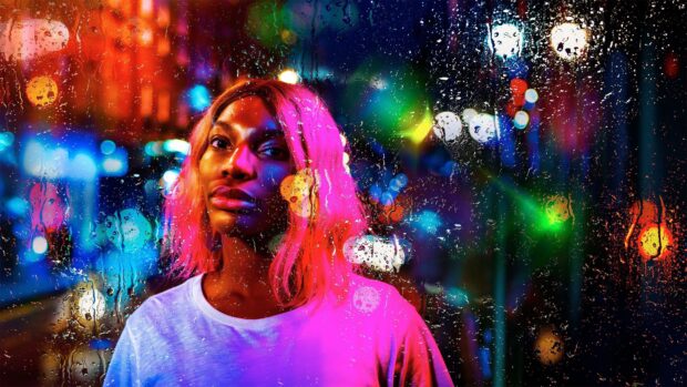 A portrait of Michaela Coel behind rain speckled glass in neon city lights, 4K Desktop Wallpaper
