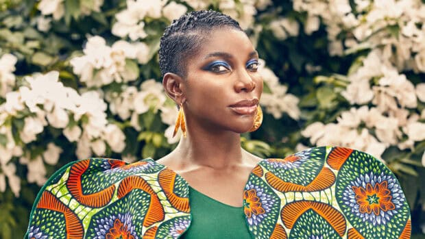 Michaela Coel wears a colorful patterned dress and blue eye makeup in an outdoor setting, HD Desktop Wallpaper