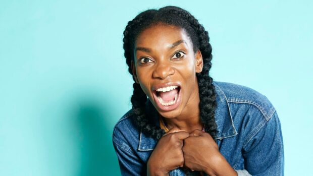 Michaela Coel is shown smiling widely with braided hair against a light blue background, HD Desktop Wallpaper