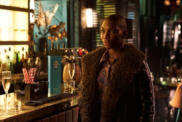 Michaela Coel stands thoughtfully inside a bar setting wearing a furry coat, 2K Desktop Wallpaper