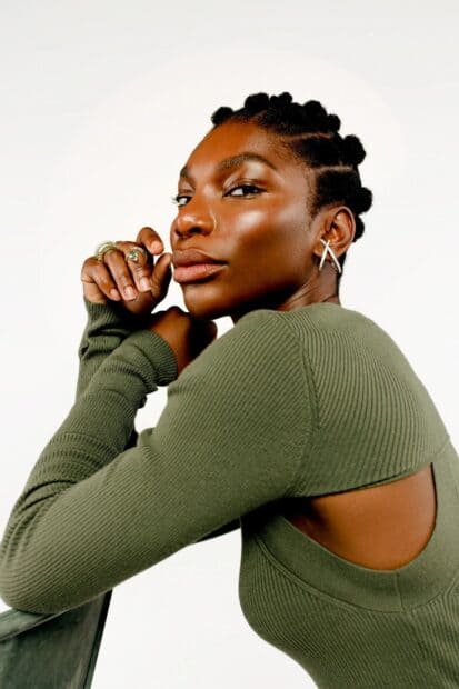 Michaela Coel poses thoughtfully wearing a green ribbed top with bold earrings, HD Mobile Wallpaper