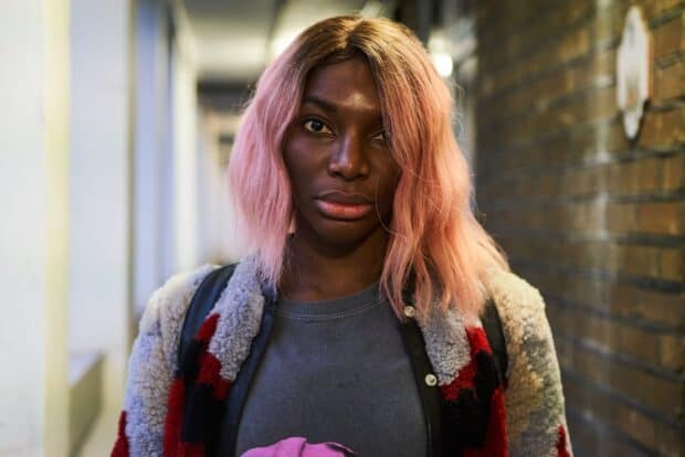 Michaela Coel looks directly at the camera with a serious expression and pink hair, HD Desktop Wallpaper