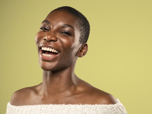 Michaela Coel is smiling joyfully in front of a plain green background, HD Desktop Wallpaper