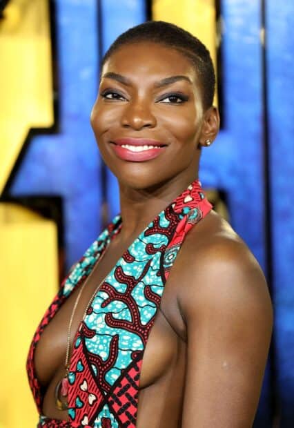 Michaela Coel smiles brightly wearing a vibrant patterned dress and gold earrings, HD Mobile Wallpaper