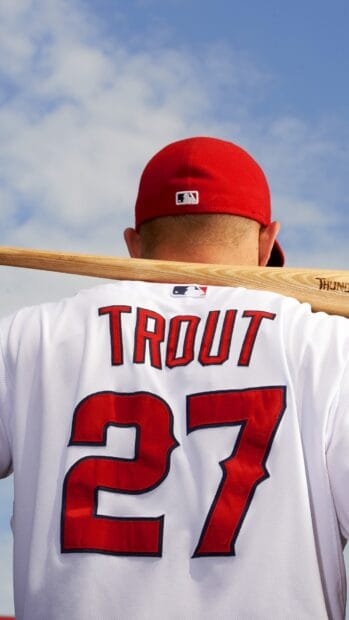 A person wearing a Mike Trout jersey holding a baseball bat on their shoulder under a cloudy sky with Los Angeles Angels wallpapers, HD Phone Wallpaper