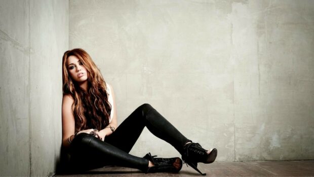 Miley Cirus sits against a concrete wall wearing black leggings and heels, HD Desktop Wallpaper