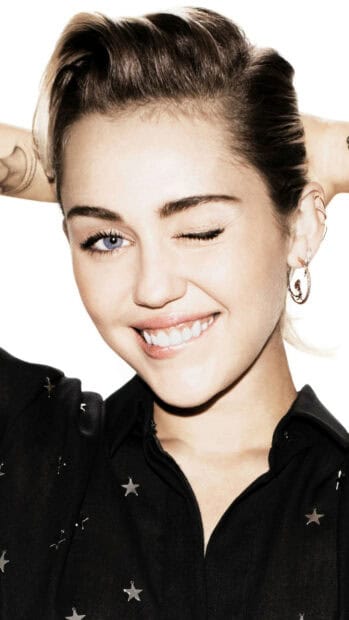 Miley Cirus smiles playfully with one eye closed wearing star decorated shirt, 2K Phone Wallpaper