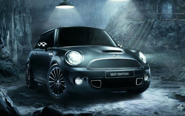 A black Mini Cooper with headlights on stands in a rocky cave environment, HD Desktop Wallpaper