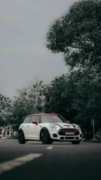 A white Mini Cooper with red mirrors and roof is parked on an empty road surrounded by trees, HD Phone Wallpaper