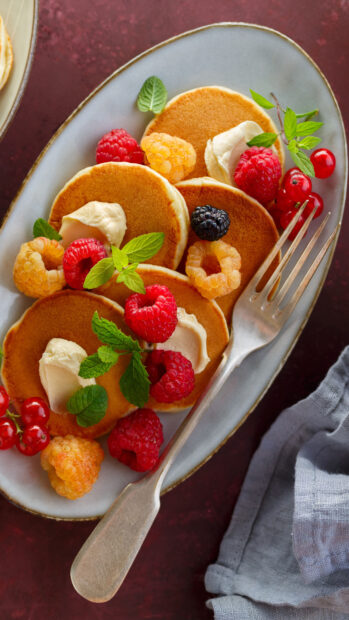 Mini pancakes with fresh berries and cream on a plate with mint leaves, 4K Phone Wallpaper