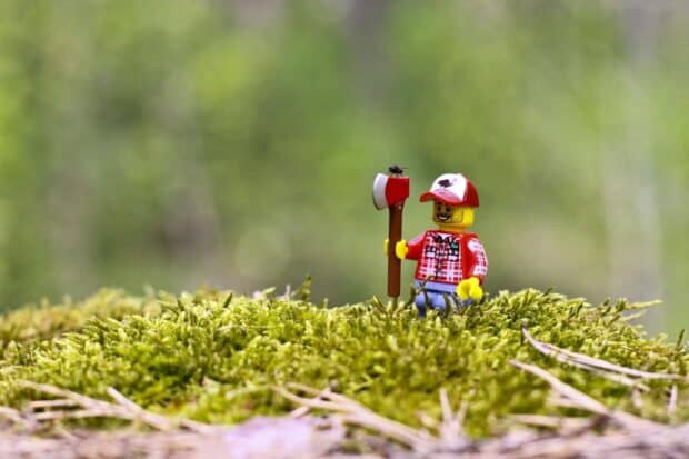 A miniature figure of a lumberjack holding an axe stands on green moss with a small insect on the axe, HD Desktop Wallpaper