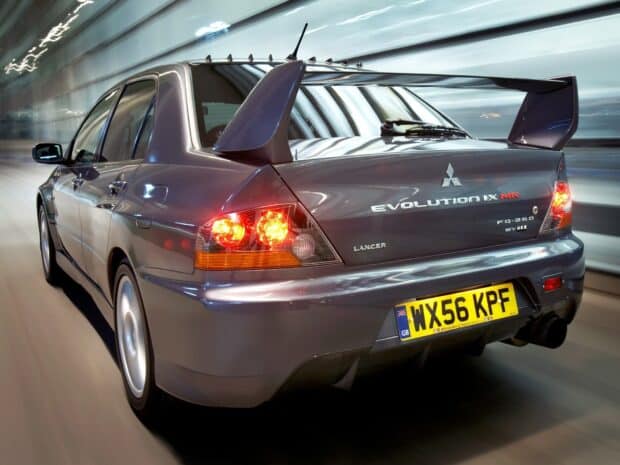 A silver Mitsubishi Lancer Evo IX is shown speeding in a tunnel with glowing rear lights, HD Desktop Wallpaper
