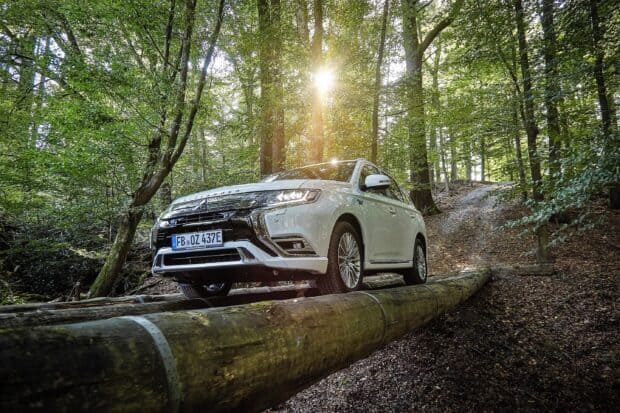 A Mitsubishi Outlander is crossing a wooden beam on a forest path with sunlight filtering through the trees, 2K Desktop Wallpaper