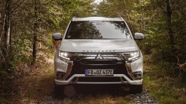 A silver Mitsubishi Outlander drives through a dense forest path surrounded by trees, 4K Desktop Wallpaper