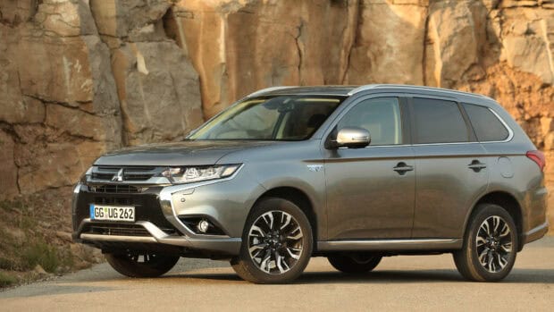 A silver Mitsubishi Outlander parked on a road near rocky cliffs with warm lighting, 4K Desktop Wallpaper