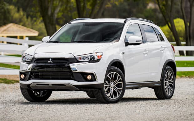 A white Mitsubishi Outlander is parked on a gravel surface with a white fence and greenery in the background, HD Desktop Wallpaper
