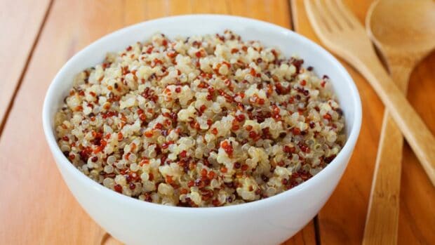 A bowl filled with mixed cooked quinoa on a wooden table with utensils, HD Desktop Wallpaper