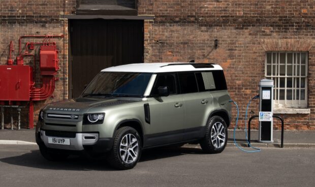 A Land Rover Defender is charging at an electric vehicle station near a brick wall, HD Desktop Wallpaper