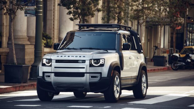 A Land Rover Defender is parked near city buildings on a sunny day, 4K Desktop Wallpaper