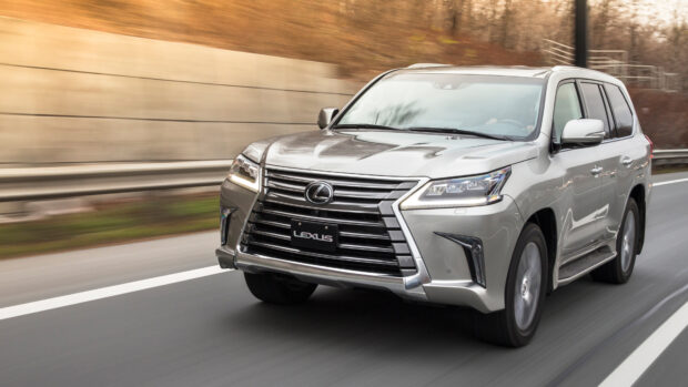 A silver Lexus LX is driving smoothly on a highway surrounded by trees and a concrete barrier, 4K Desktop Wallpaper